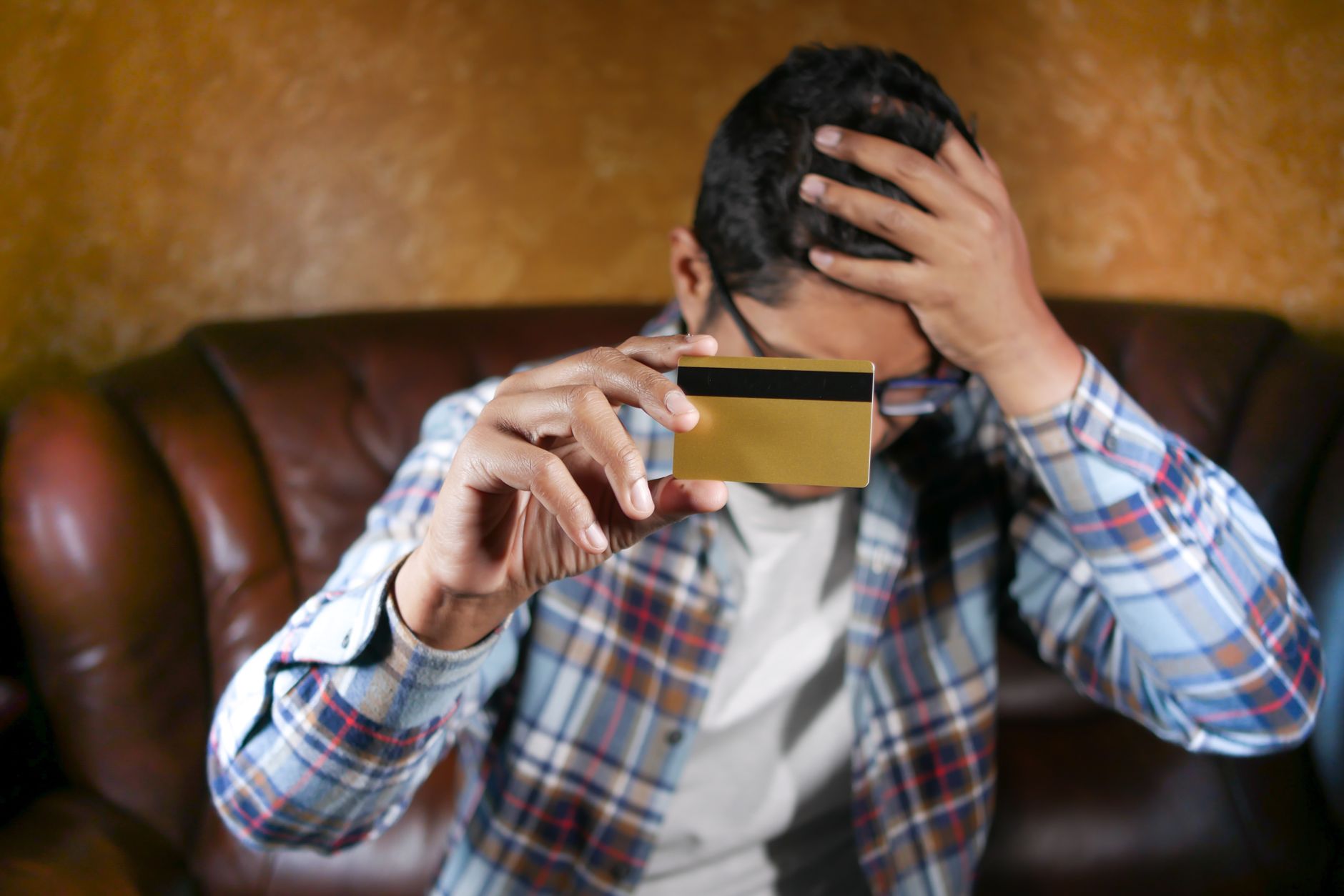 Man on his couch holding a credit card and looking worried about his balance
