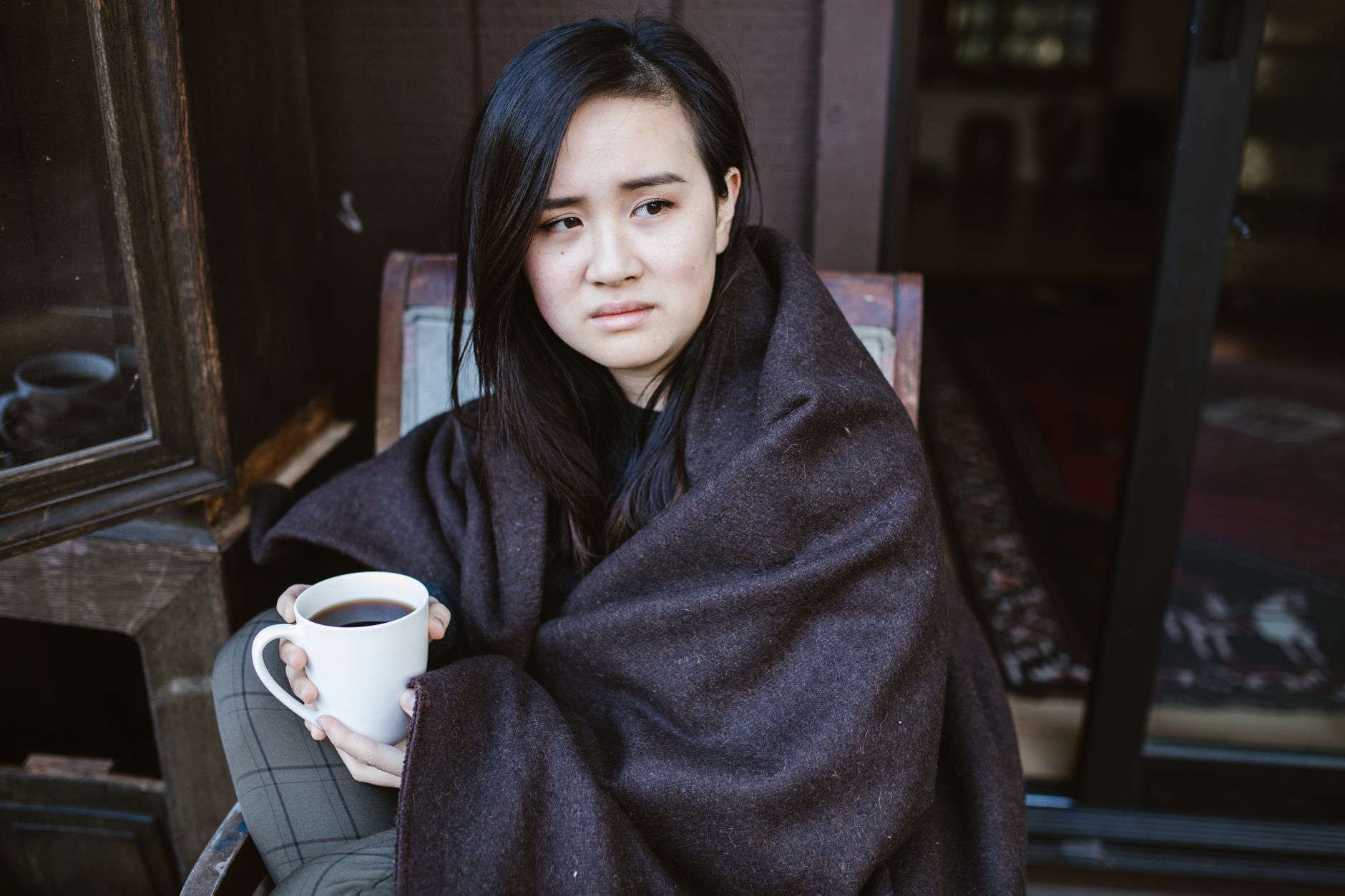 Woman wrapped in a blanket with a warm drink at home during a cold month