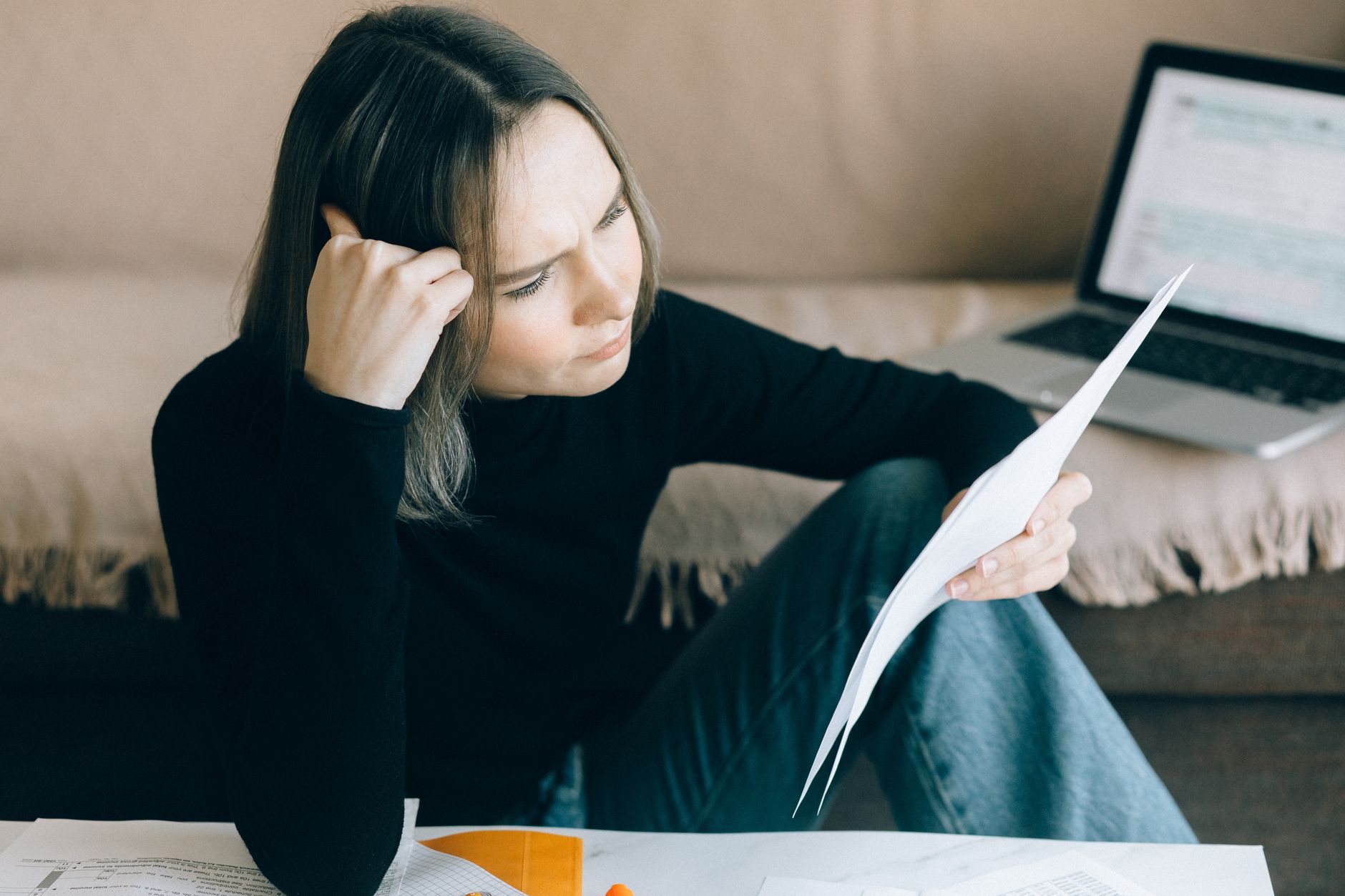 Woman comparing bill due dates on paper with her bank account on a laptop