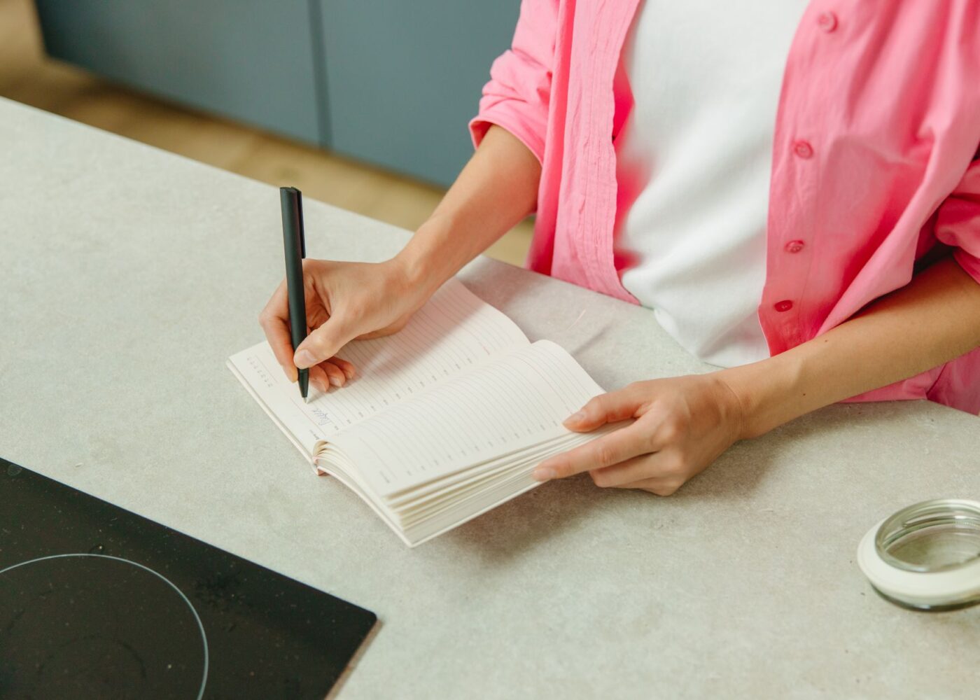 Woman writing a list of upcoming holiday and insurance bills in a notebook at her kitchen counter