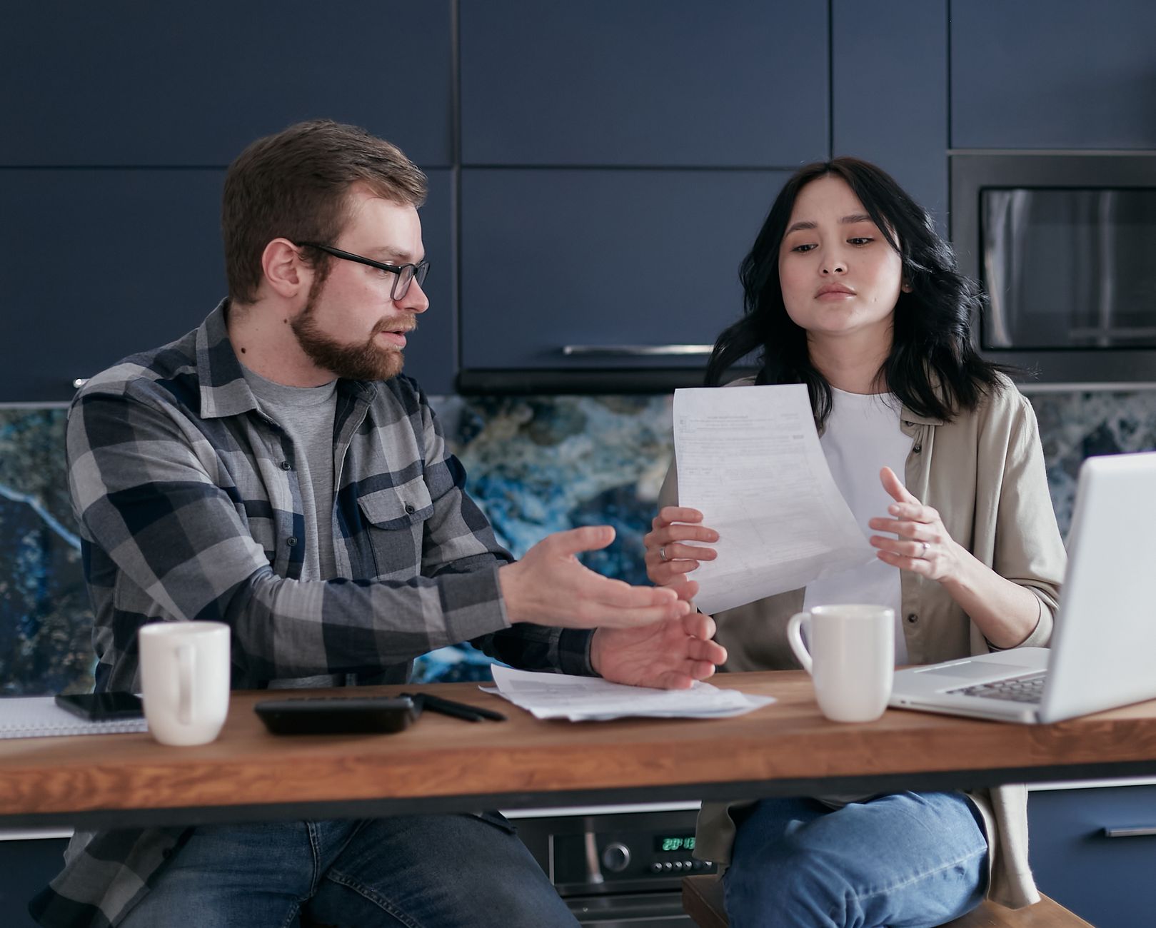 A couple reviews bank and credit card statements at their kitchen table