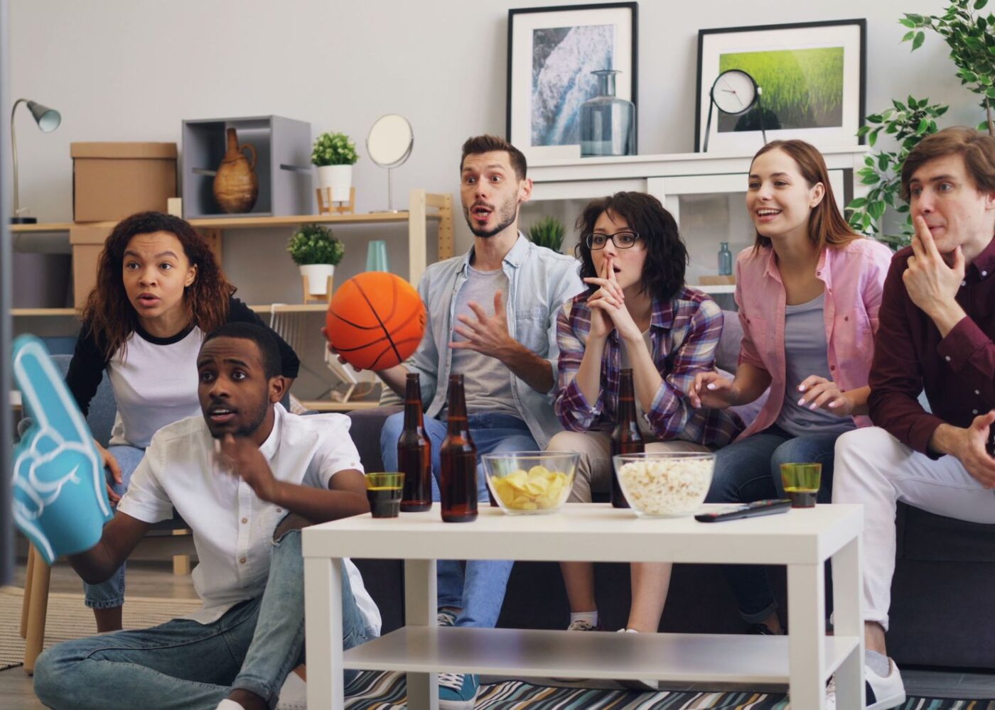 Friends watch a college basketball game together while one checks a sports betting app on his phone