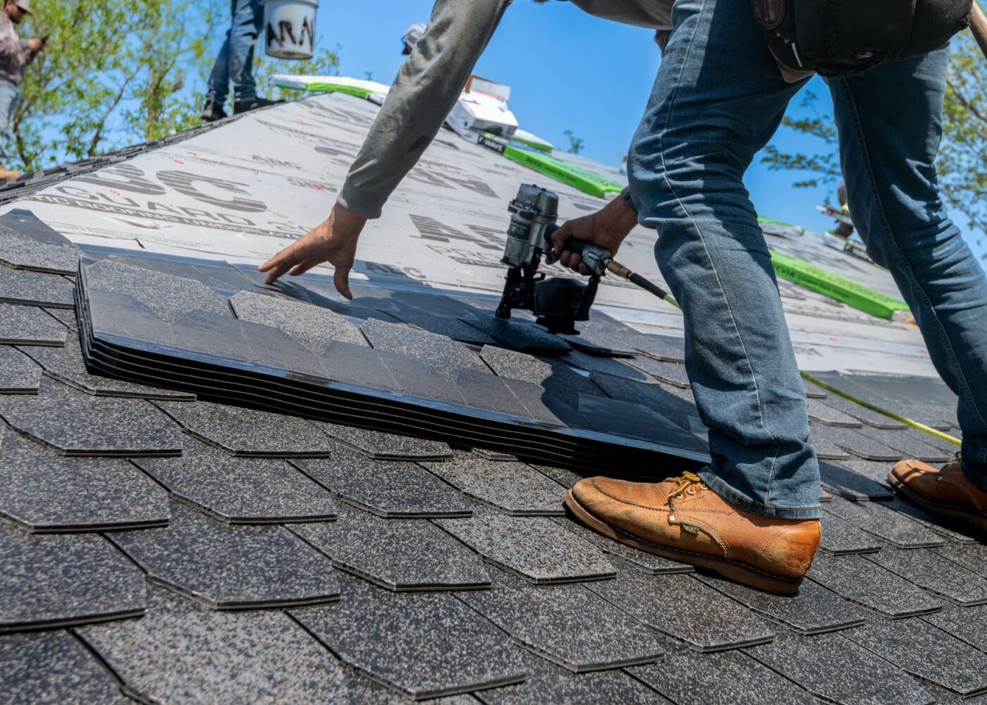 Roofer inspecting asphalt shingles for hail damage after a spring storm